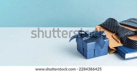 Happy Fathers Day background banner. Side view. Blue gift box and brown paper bag, necktie and agenda on pastel blue table. Corporate gift Royalty-Free Stock Photo #2284386425