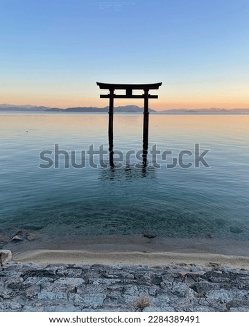 A large Torii gate on Lake Biwa in Japan located next to the Shirahige Shrine at sunset. Translation of the Kanji to English: Shirahige Jinja