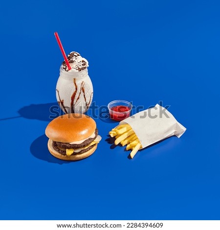Combo meal with burger, fries, sauce, and milkshake on a blue background. Minimalist fast food photography featuring hard shadows, a bright blue backdrop, and a modern style Royalty-Free Stock Photo #2284394609
