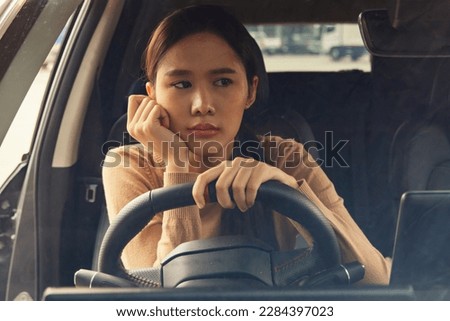 Woman driving alone negative emotions : Asian woman with her hands on her chin feeling overwhelmed tired stressed out at work overthinking and absent minded in the car while driving distracted driving Royalty-Free Stock Photo #2284397023