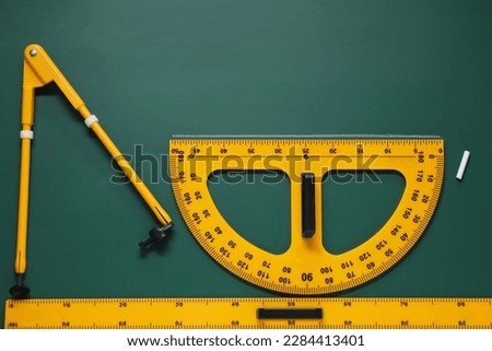 Protractor, compass, chalk and ruler on green chalkboard, flat lay