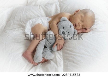 Sleeping newborn baby hugging a teddy bear.