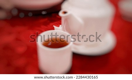 Blurred or Not Focused Background Of Chinese Tea or Japanese Tea Served in a White Teapot and Small Mini Ceramic Cups on a Round Table with Red Cloth. Chinese Menu. High Quality Photography Background