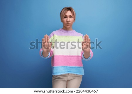 pleasant blond woman in casual outfit showing stop sign on blue background with copy space