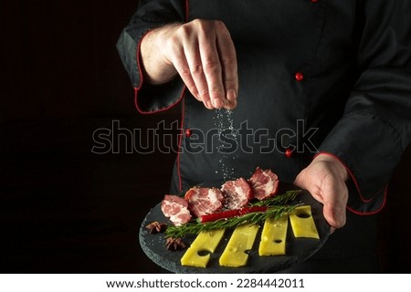 The chef sprinkles salt on a sliced steak with ham and cheese on a serving plate. The concept of serving dishes to order by a waiter with space for a menu on a black background.