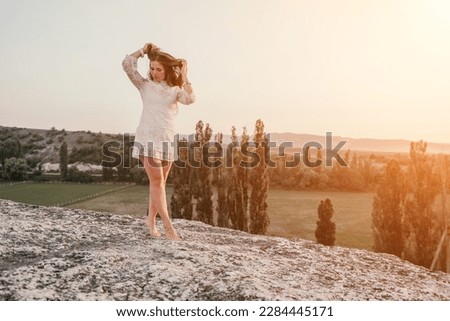 Happy woman in white boho dress on sunset in mountains. Romantic woman with long hair standing with her back on the sunset in nature in summer with open hands. Silhouette. Nature. Sunset.