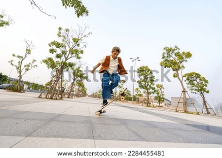 Young Asian man skating on longboard skate at park on summer holiday vacation. Handsome guy enjoy and fun urban active lifestyle practicing outdoor sport skateboarding on city street at sunset.