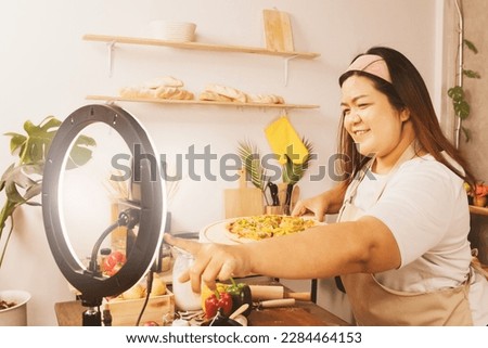 Fat female streamer presents cooking contents homemade pizza in the kitchen at home teaching how to make pizza easily recording on online business streamer platforms video clips audio clips pictures.