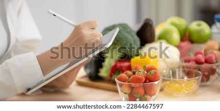 Panoramic of hand professional nutrition healthful surrounded by a variety of fresh fruits and vegetables working on digital tablet. Concept of right nutrition, diet and healthcare. Royalty-Free Stock Photo #2284467597
