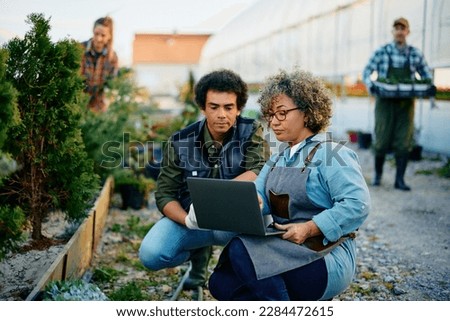 Female quality control manager and worker using laptop while working at plant nursery. 