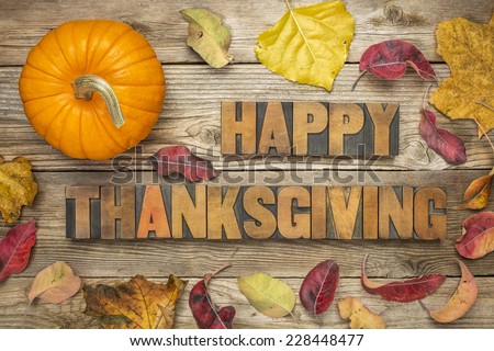 Happy Thanksgiving  - text in vintage letterpress wood type blocks against rustic wood background with a pumpkin and dry leaves