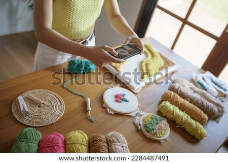 Asian Woman taking smartphone photo Punch needle. phone posting on social networks in studio workshop. designer workplace Handmade craft project DIY embroidery. Royalty-Free Stock Photo #2284487491