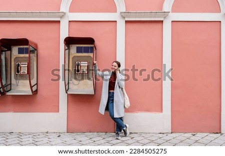 Woman standing next to the street payphone and talking on mobile phone. Royalty-Free Stock Photo #2284505275