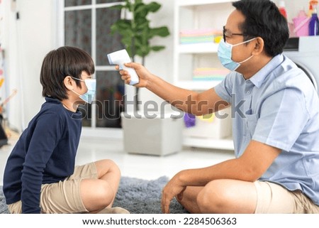 Portrait of happy love asian family mature father and little boy son wearing protective mask with social distancing use infrared forehead thermometer for checking body temperature scan fever, sick Royalty-Free Stock Photo #2284506363