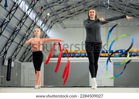 Little girl, child, rhythmic gymnast training indoors with coach, doing exercise with ribbon. Concept of sportive lifestyle, childhood, education, health, professional sport, championship