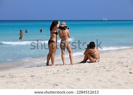 Women in bikini sharing their impressions standing with smartphones on tropical sandy beach. Photo shooting by ocean coast, vacation and travel