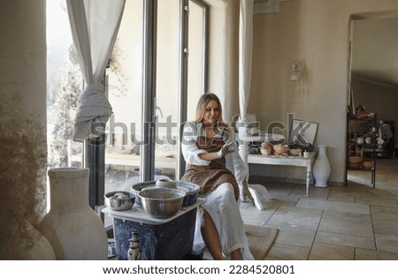 a potter girl looks at her hands while sitting behind a potter's wheel