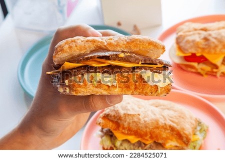 Philly cheese steak sandwich holding in hand with other sandwiches in background.  Royalty-Free Stock Photo #2284525071