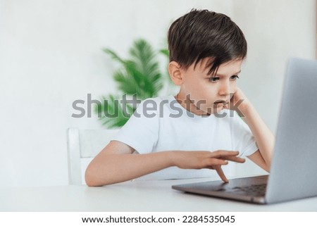child sits with a laptop at a table in a room with a green plant
