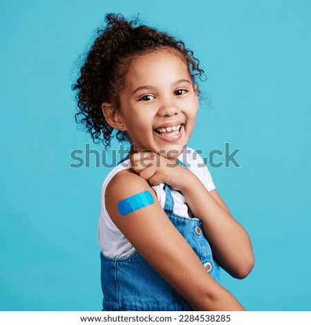Portrait, smile and girl with plaster, wellness and safety with kid against a blue studio background. Face, young person and female child with happiness, band aid and vaccine with protection and care