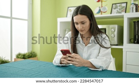 Young beautiful hispanic woman using smartphone sitting on table at dinning room
