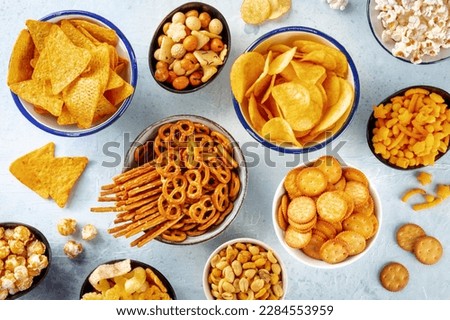 Salty snacks, party mix. An assortment of crispy appetizers, overhead flat lay shot. Potato and tortilla chips, crackers, popcorn etc Royalty-Free Stock Photo #2284553959