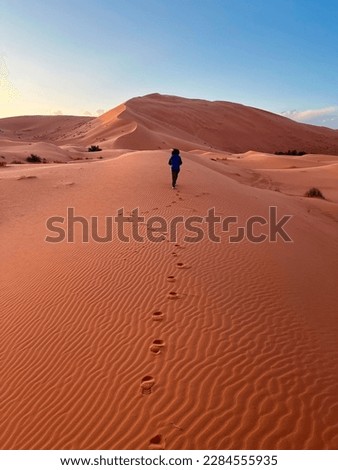 Dunes in the Sahara desert, Merzouga desert, grains of sand forming small waves on the dunes, panoramic view. Setting sun. Morocco. Girl that walk on a sand dune. Shoe prints