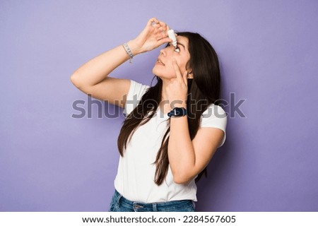 Caucasian sick caucasian woman using eye drops for her tired red eyes in front of a purple background Royalty-Free Stock Photo #2284567605