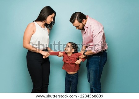 Divorced couple fighting about child custody and trying to take their scared young daughter in front of a blue background Royalty-Free Stock Photo #2284568809