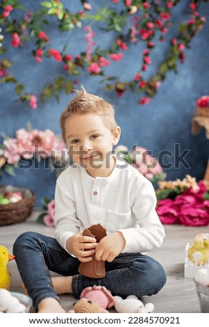Cute stylish toddler child, boy with white shirt, playing with eggs and chocolate bunny on Easter decoration, studio shot