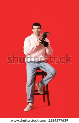 Young male photographer with professional camera sitting on red background