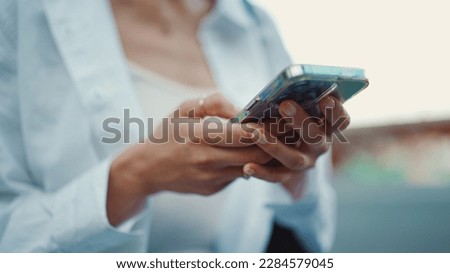 Closeup of young woman holds smartphone in her hands and scrolls through the news feed. Close-up of girl hand uses mobile phone outdoors Royalty-Free Stock Photo #2284579045