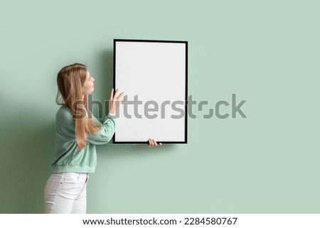 Young woman hanging blank frame on green wall