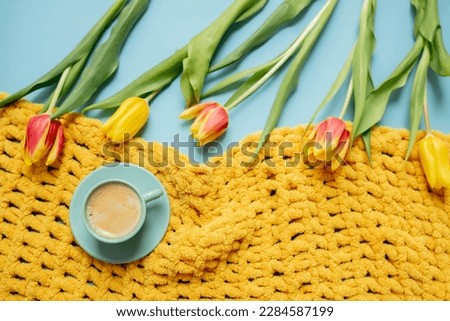 bouquet of yellow tulips, coffee in a blue cup and a yellow cozy plaid on a pastel blue background. copy space. flat lay. place for text. frame mockup