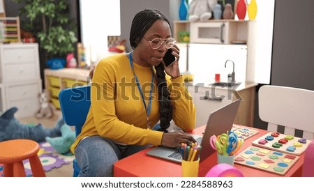 African woman preschool teacher using laptop speaking on the phone at kindergarten