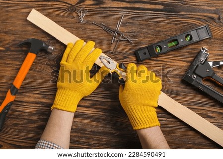 Man with pliers pulling out nail from wooden plank on table Royalty-Free Stock Photo #2284590491