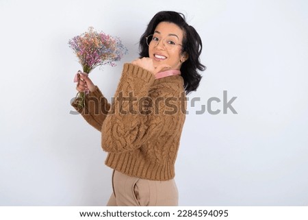 Hooray cool beautiful woman holding a bouquet of flowers wearing knitted sweater over white background point back empty space hand fist