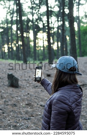 latina woman with cap and jacket taking a selfie with cell phone in a forest in autumn