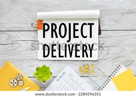 PROJECT DELIVERY notepad with clip and text near keyboard calculator and glasses