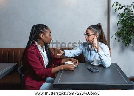 Two young women business partners, owners of a small company, new to the market, a job break in a coffee shop, talking and drinking coffee, making plans for the future and developing business tactics