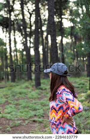 latina woman with multicolored cap and sports jacket in profile looking at a forest. vertical picture