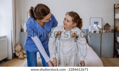 Young nurse helping to walk to little girl with broken leg.