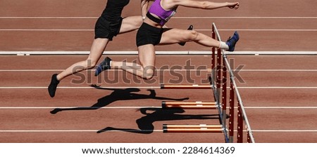two female athletes running hurdles in athletics competition, hurdling on stadium track, summer sports games Royalty-Free Stock Photo #2284614369