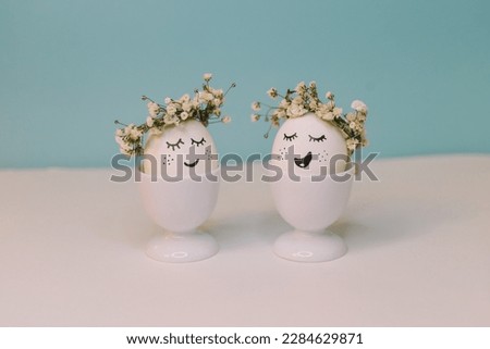 A white egg with a face made of flowers sits in an egg shell with a yellow flower on it.