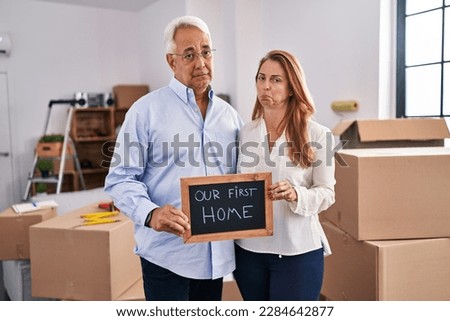 Middle age hispanic couple moving to a new home holding banner depressed and worry for distress, crying angry and afraid. sad expression. 