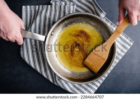 Brown Butter in a Stainless Steel Skillet with a Wooden Spatula: Overhead view of browned butter being stirred in a frying pan Royalty-Free Stock Photo #2284664707