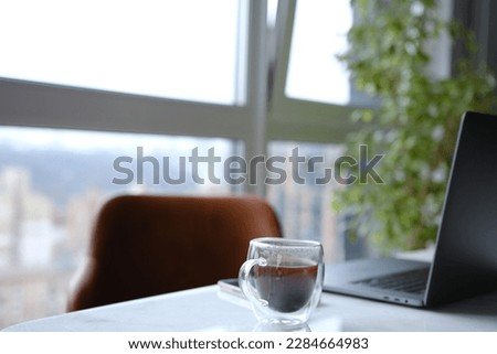 workplace with laptop and transparent cup of coffee in home office on white marble desk with brown leathern chair and green tree at background with window Royalty-Free Stock Photo #2284664983