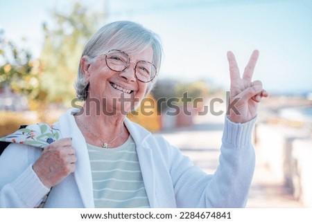 Portrait of smiling senior caucasian woman in outdoors looking at camera gesturing positive sign, enjoying sunny day, vacation or retirement concept