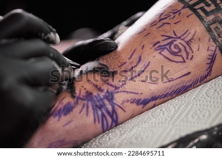 Close up tattoo machine. Tattooing. Man creating picture on his arm by a professional tattoo artist.