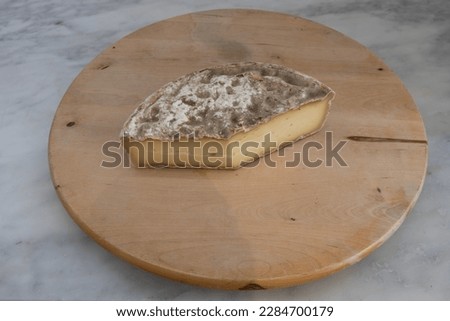 French culinary Still Life. Piece of cheese Tomme de Savoie placed on a wooden pan